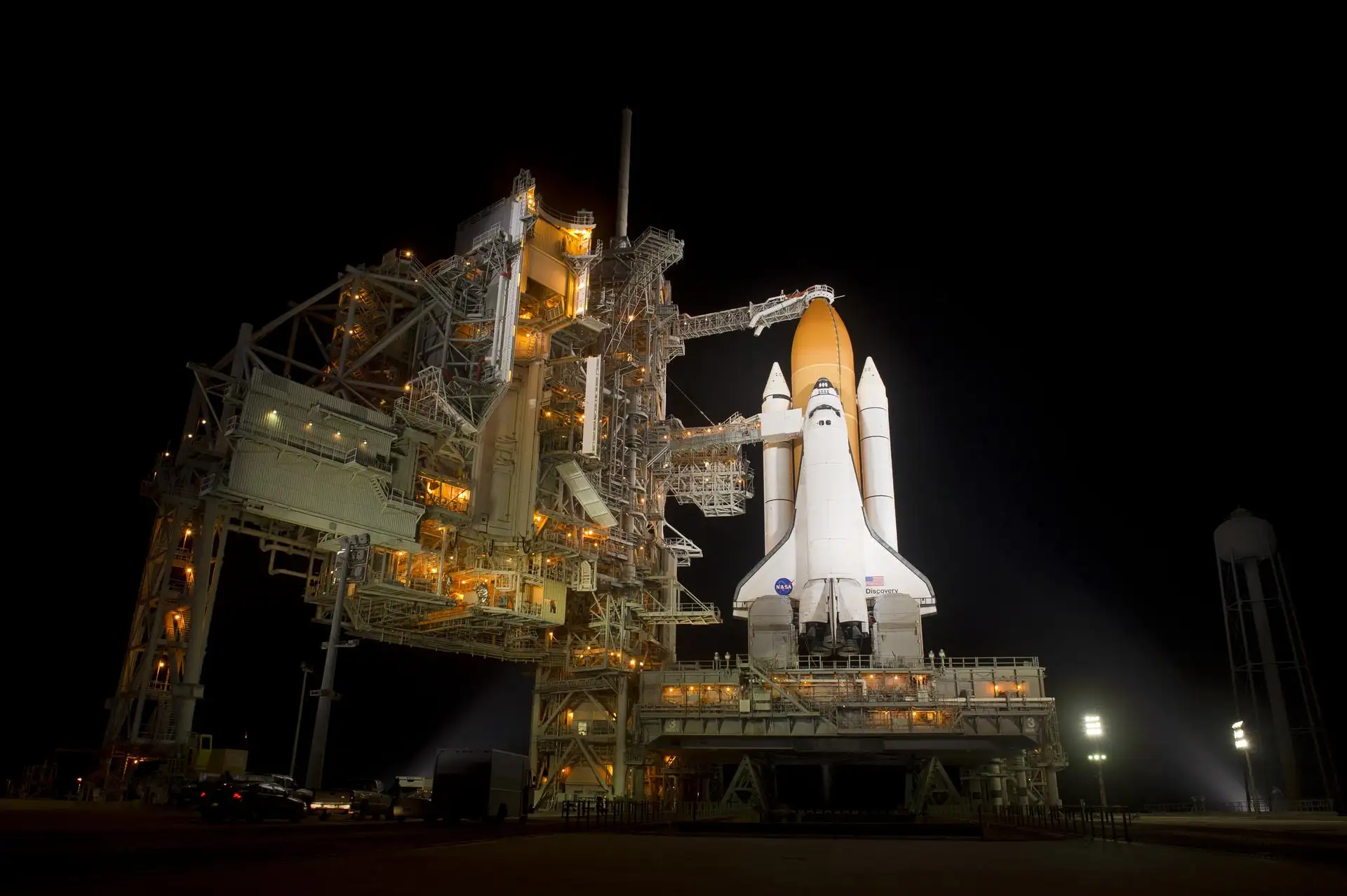 航天飞机在发射台的夜景，巨大的外部储箱和固体火箭助推器被泛光灯照亮